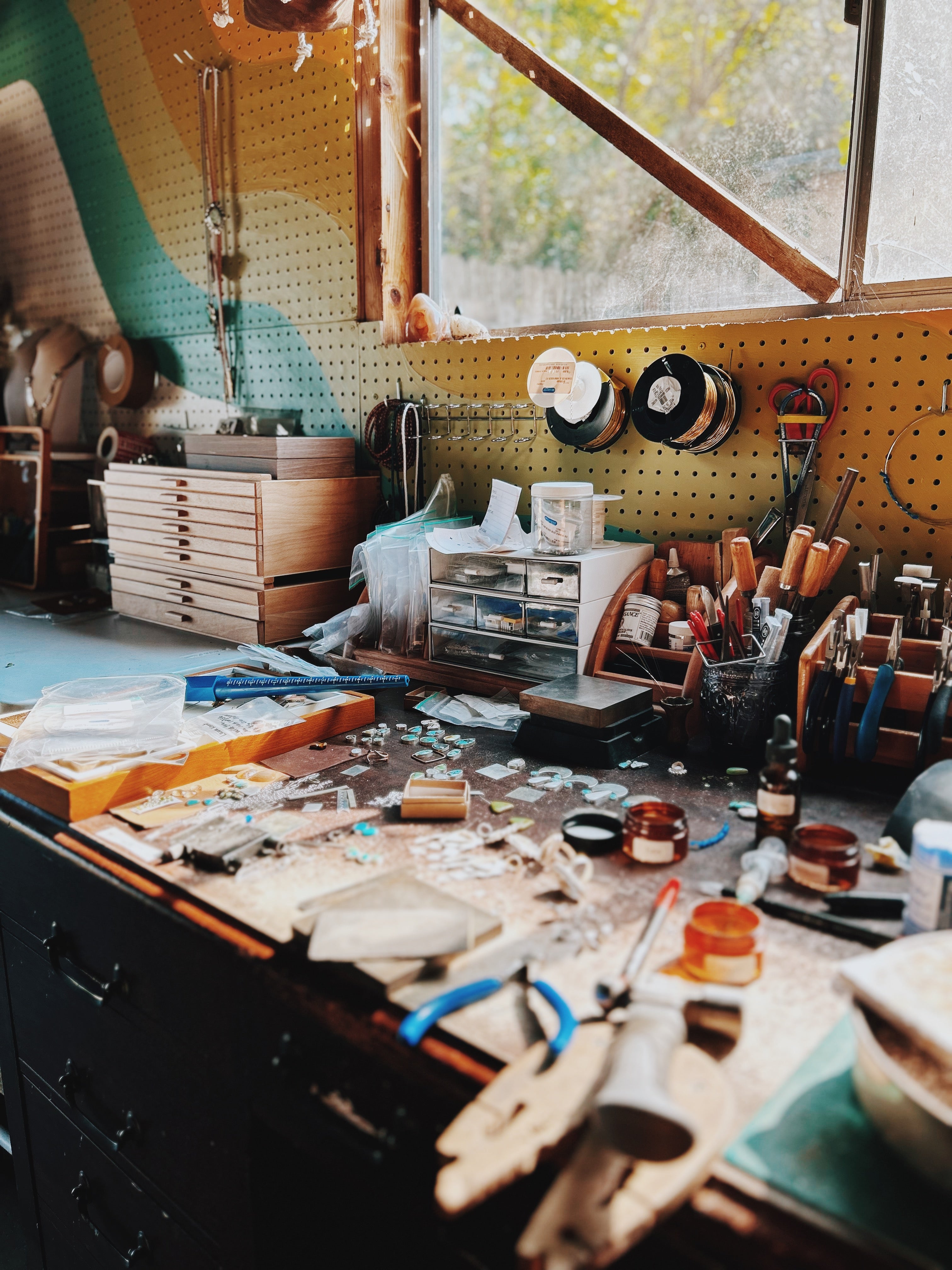Workshop with tools and materials on a table, pegboard wall with tools, and window view.