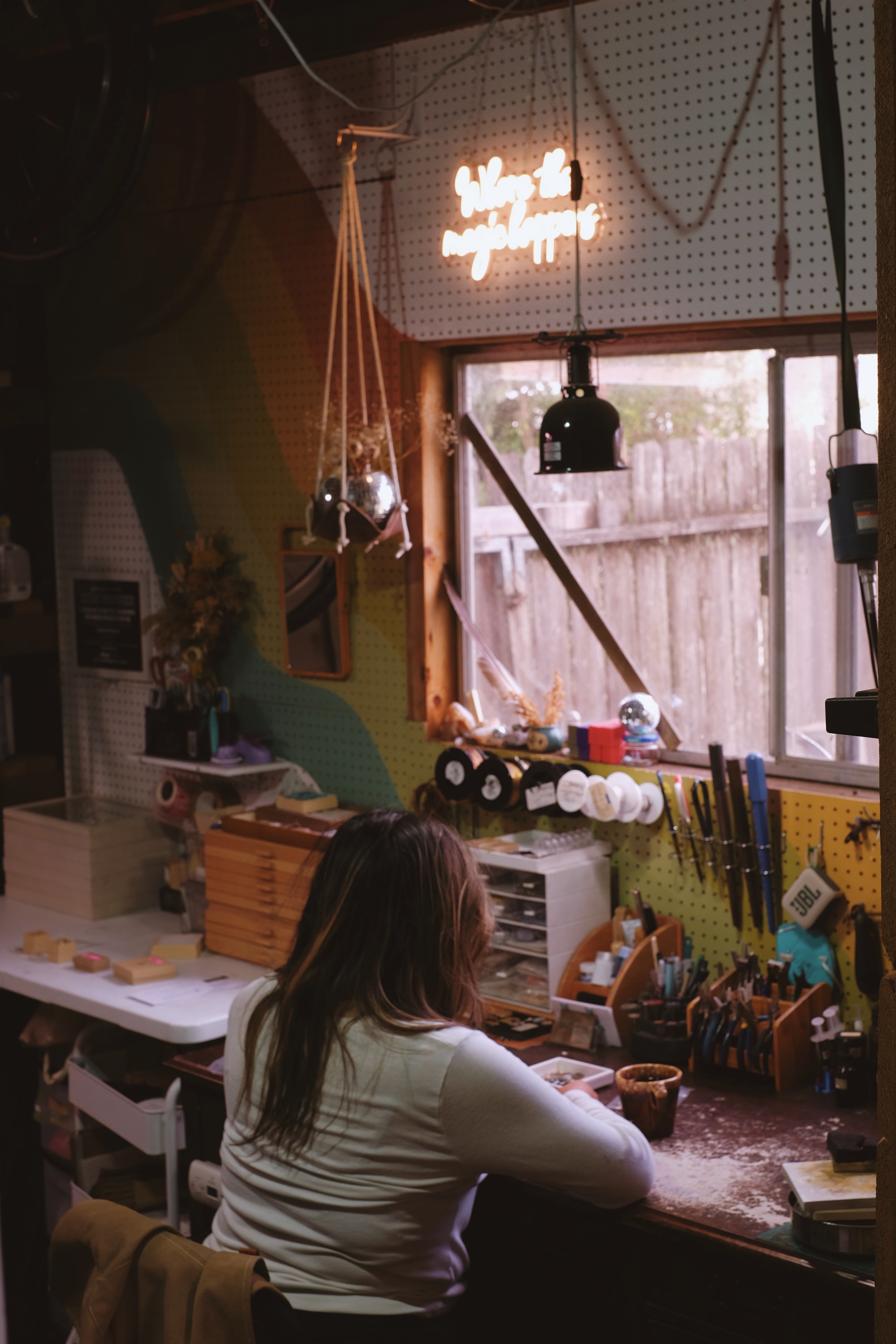 Person sitting at a table in a workshop with various tools and equipment.